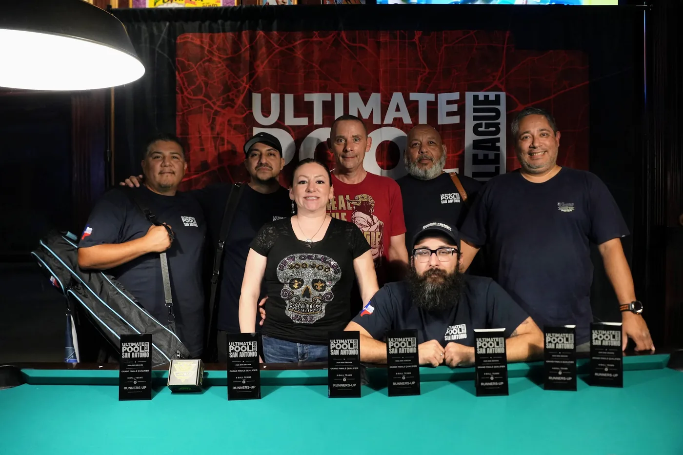 The Lucky 8 behind their row of Runners-Up trophies in front of the Ultimate Pool League backdrop at Fast Eddie's Braun.