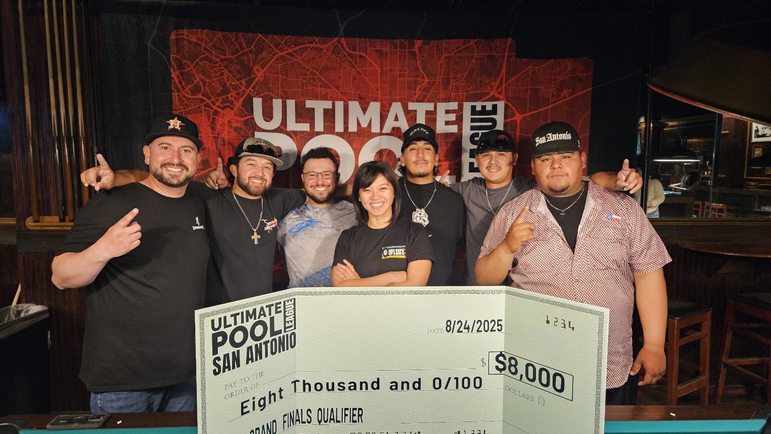 Last year's 8-Ball Grand Finals Qualifier winners and the league operator holding an $8,000 travel fund check at Fast Eddie's Braun, dated August 24, 2025.